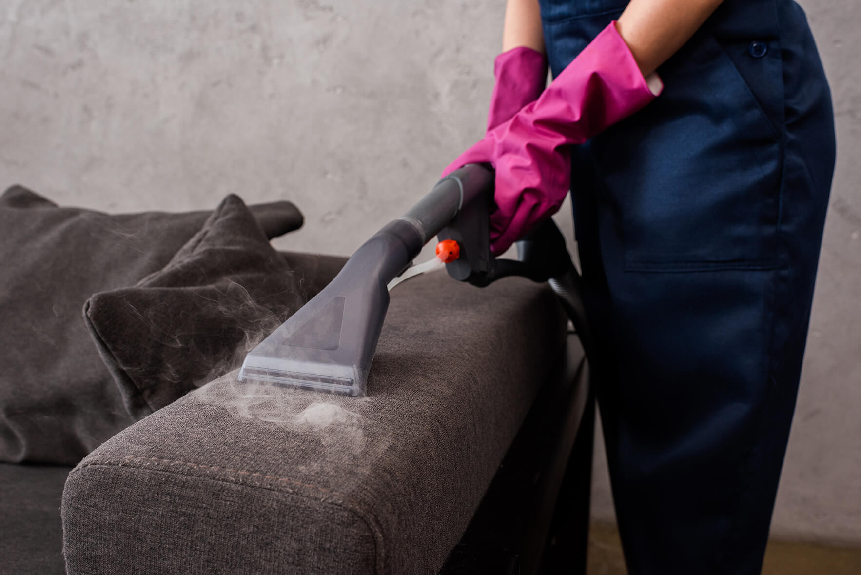 A technician with rubber gloves steam cleaning upholstery of a couch